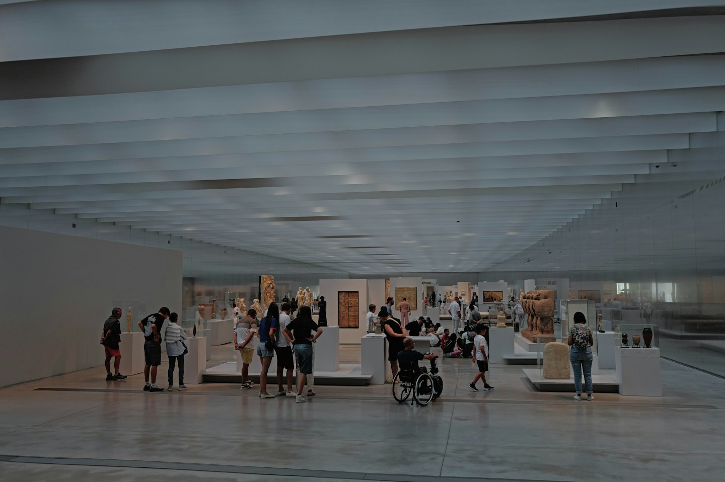 Museum visitors examining historical artifacts in a bright, modern gallery.