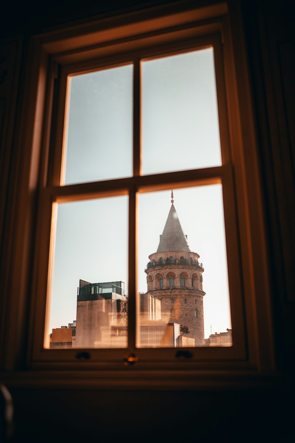 Historic stone tower with conical roof seen through a wooden window.
