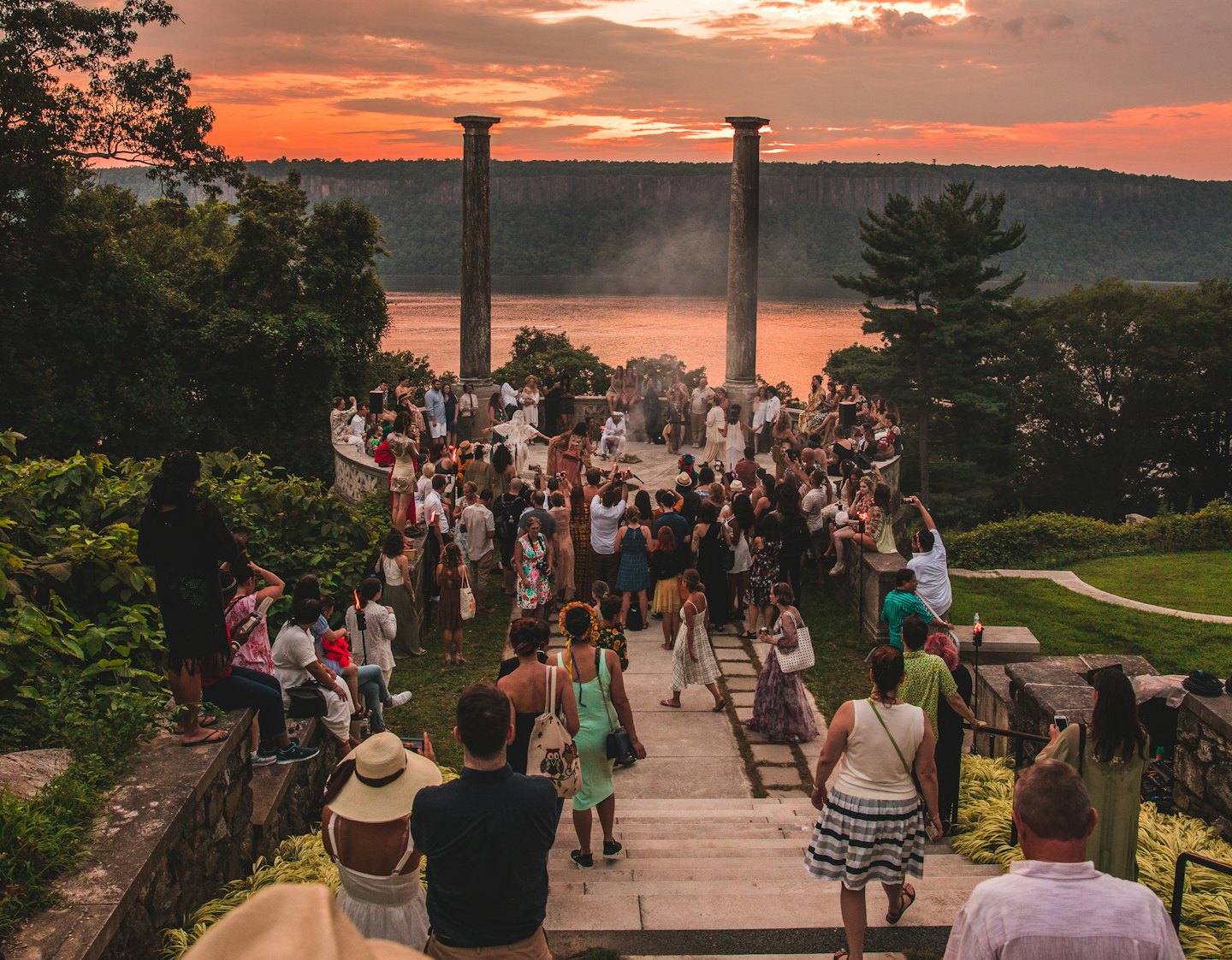 People gather on a stone terrace at sunset by a river.