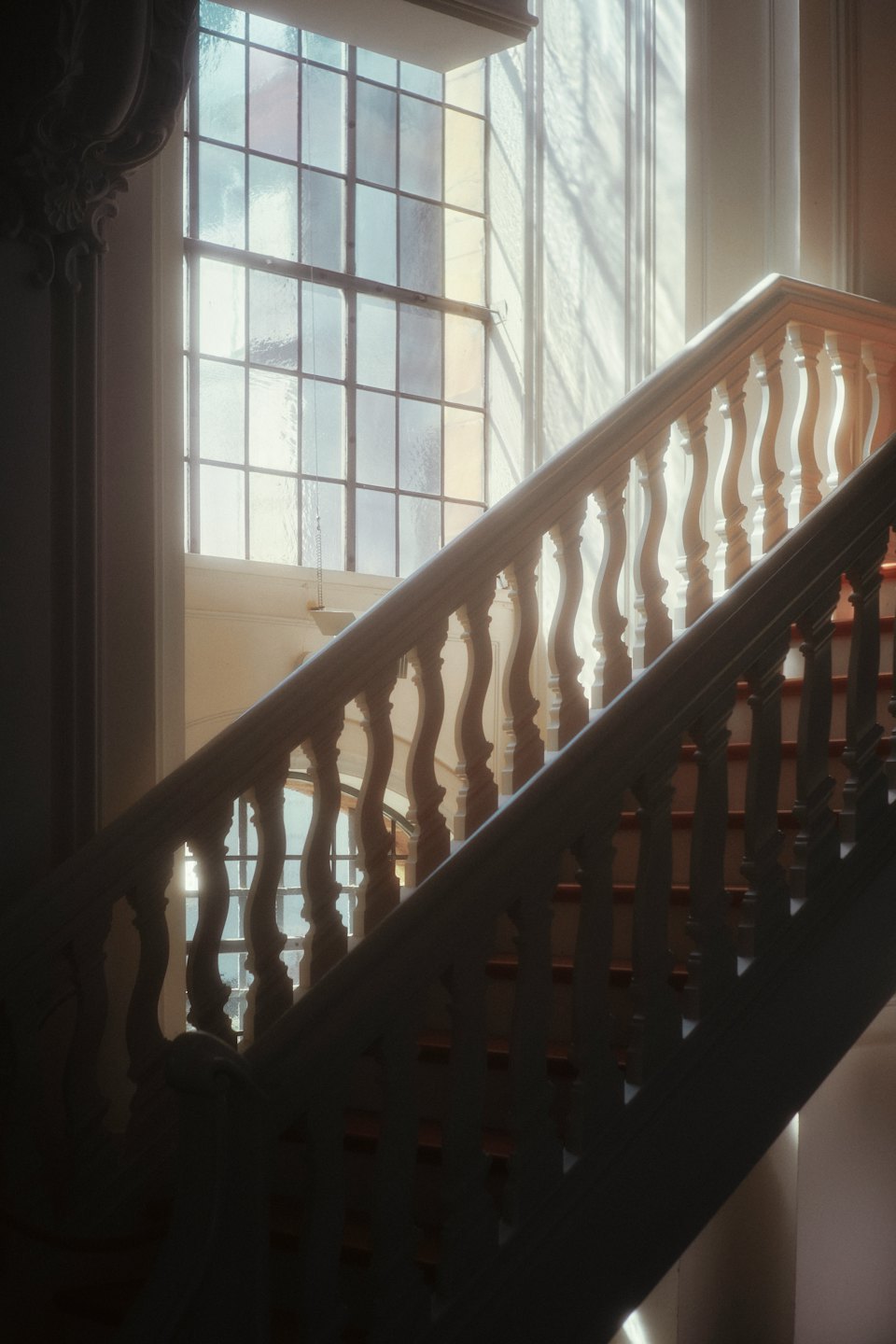 Grand staircase with ornate balusters ascends toward a large window.