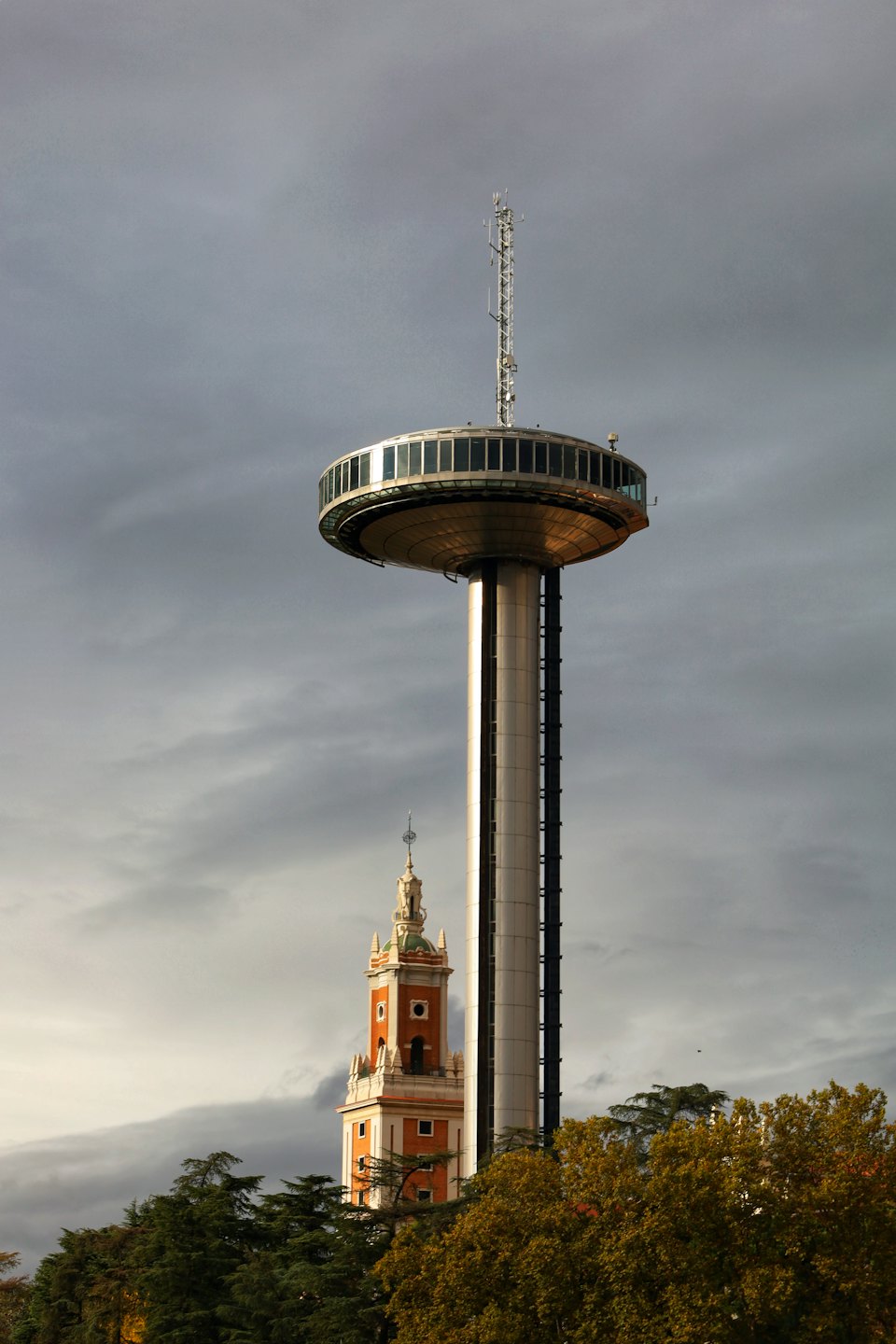Modern cylindrical observation tower standing beside a historic brick building.